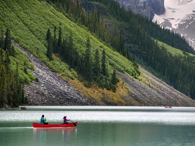 A couple in a red canoe paddle across a lake with the lower slopes of a mountain in the background