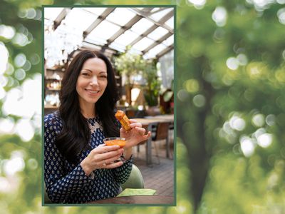 Actor Laura Prepon smiling at the camera and holding a piece of cheese.