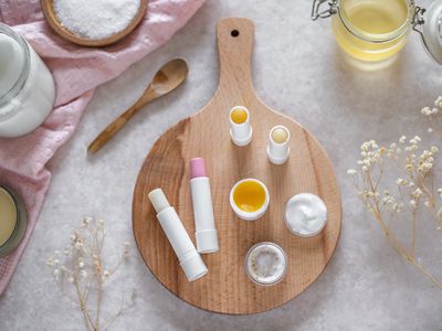 natural lip care products arranged on circle cutting board with flowers