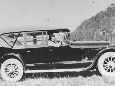 A vintage photo of a 1920s car with a woman driver