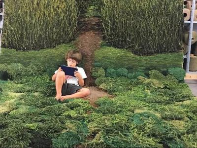 Child reading a book inside on a rug that looks like meadow