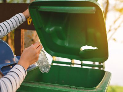 Cropped hands of a person throwing a bottle in a green recycling bin.