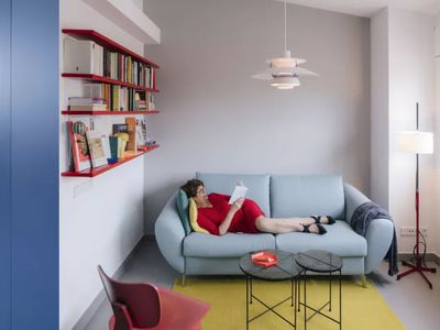 Woman in a red dress read while lounging on a blue sofa in a modern apartment