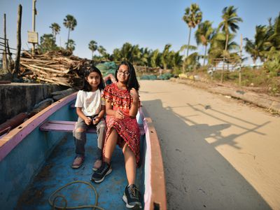 two young girls sitting in a fishing boat on rural Indian shoreline