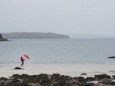 Person with umbrella at windy beach, Isle of Skye, Scotland