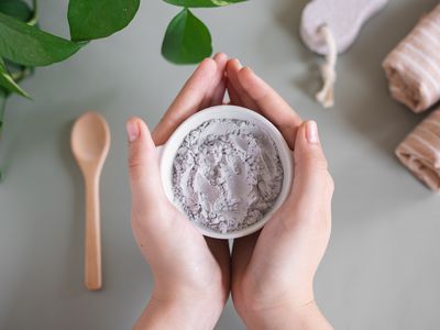 two hands hold gray bentonite clay in bowl for beauty treatments