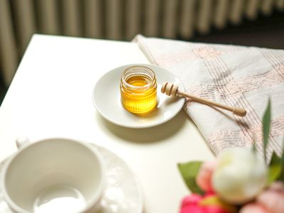 jar of honey with wooden dipper sits on table with flowers