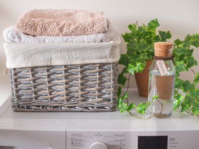 washing machine with glass bottle of vinegar, laundry basket with towels, and ivy plant