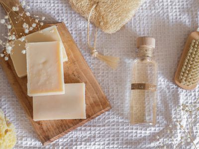 bars of soap and liquid castile soap display on white waffle fabric with wooden brush and loofah