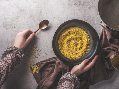 Woman hands holding bowl with uncooked millet on dark concrete background.