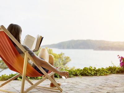 Woman reading book while relaxing on deck chair