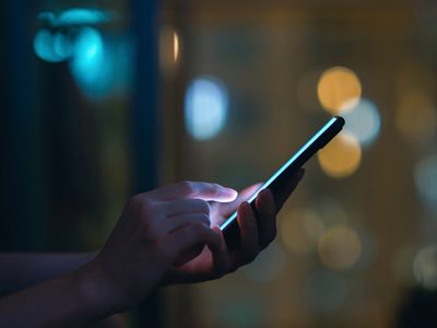 Close up of woman's hand using smartphone in the dark, against illuminated city light bokeh