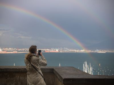 woman photographs rainbow of city of Naples, Italy