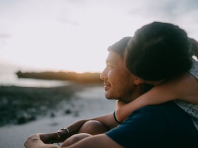 Young daughter embracing her father from behind on beach