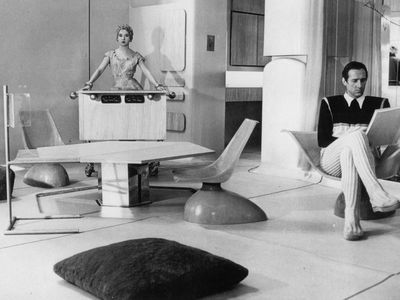 Black and white photo of a man and woman in a room with angular, futuristic furniture